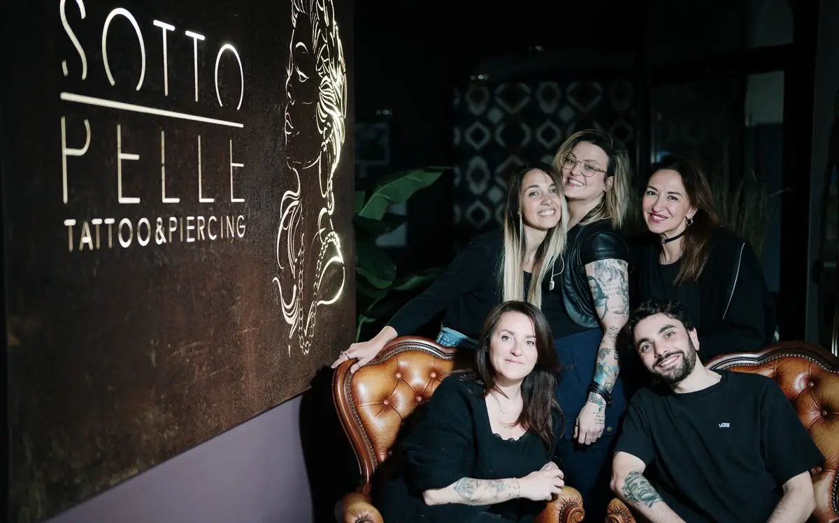 Il team di Sottopelle sui divani in pelle, accanto all'insegna illuminata dello studio